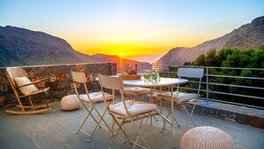 A terrace with a table and chairs, overlooking a mountainous landscape during sunset.