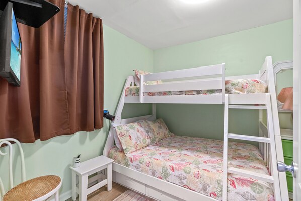 Un lit superposé avec une literie à motifs floraux, une petite table de chevet, une chaise et un rideau.
