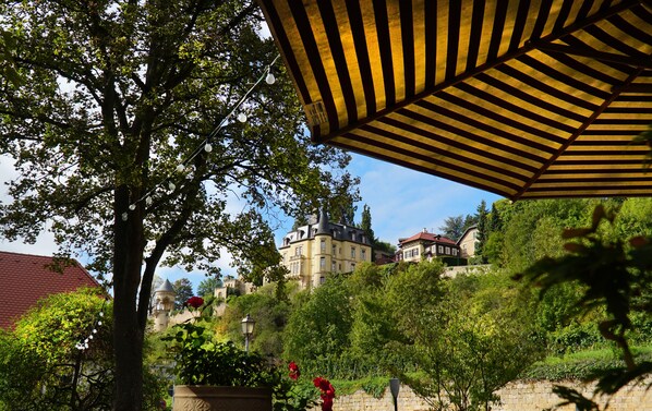 Vista de un edificio histórico con techo rojo, rodeado de exuberante vegetación y un muro de piedra.