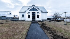 En hvid bygning med en midterdør og to vinduer til hver side, omgivet af græs og en belagt sti, der fører hen til den.