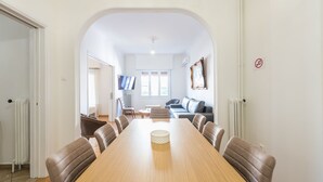 Un comedor amplio con una larga mesa de madera y sillas de cuero, que conduce a una sala de estar con un sofá y una televisión.