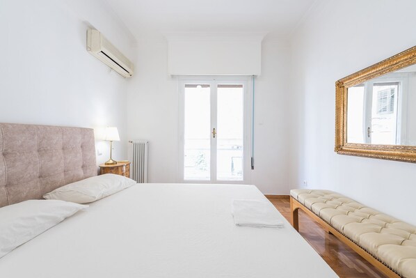 A hotel room with a large bed, a bench, a mirror, and a window with a view.
