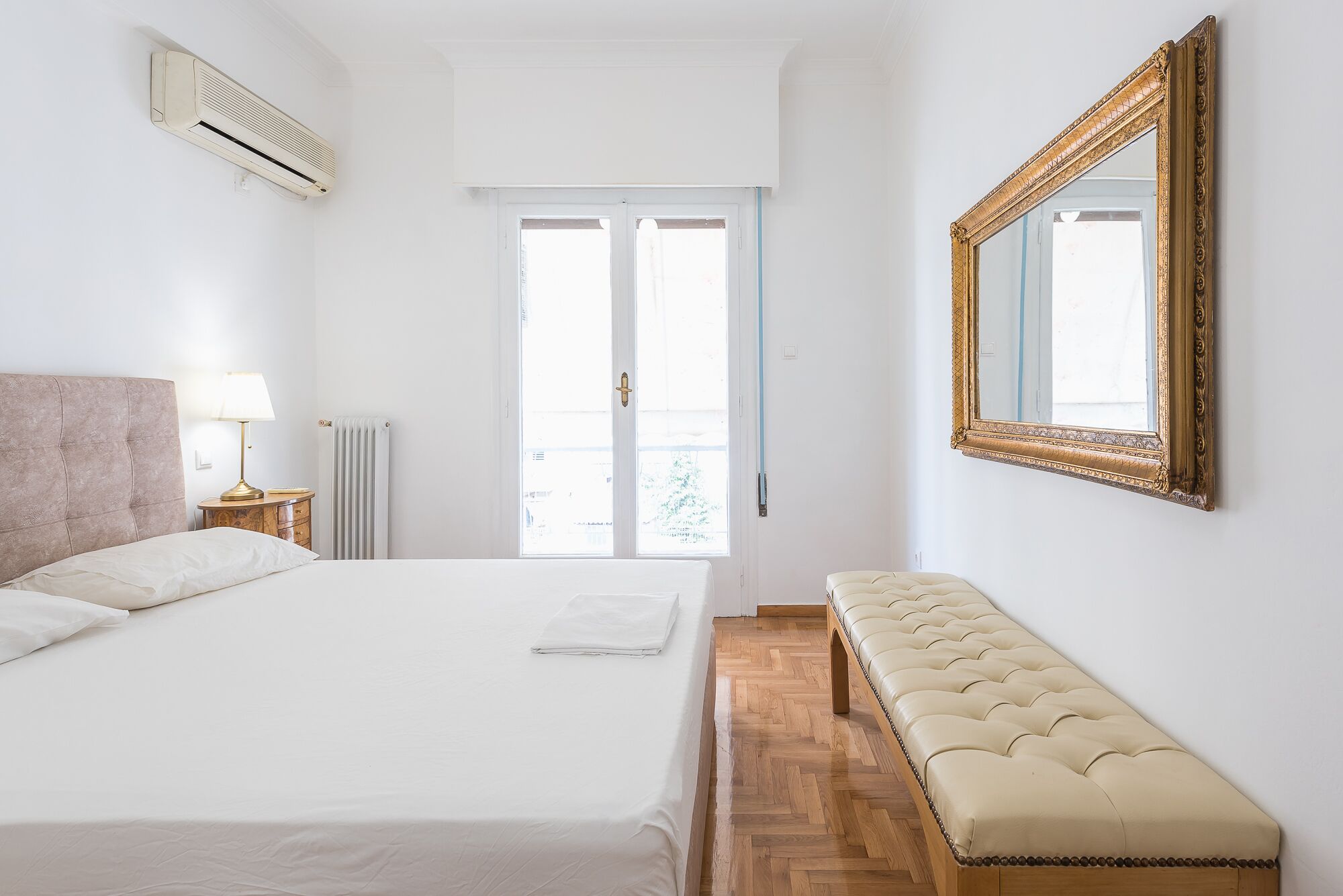 Ein Schlafzimmer mit Bett, Nachttisch, Lampe, Heizkörper und einem großen Spiegel.
