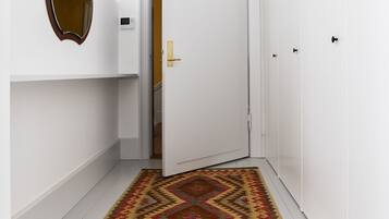 A hallway with white walls, a patterned rug, a mirror, and a door leading to another room.
