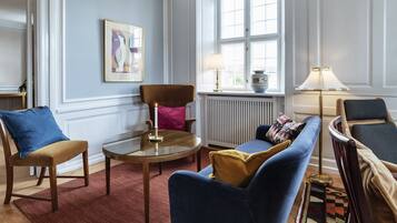 A living room with a round coffee table, two armchairs, a sofa, a radiator, and a window with a view.