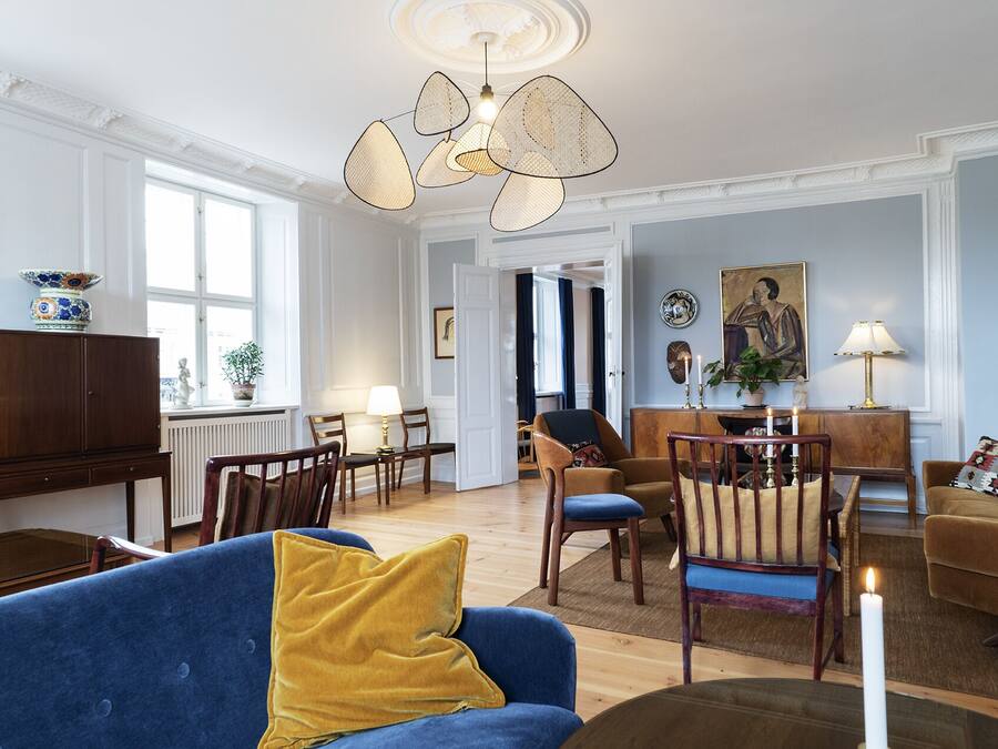 A spacious living room with a blue sofa, wooden chairs, a coffee table, and a dining area with a table and chairs.