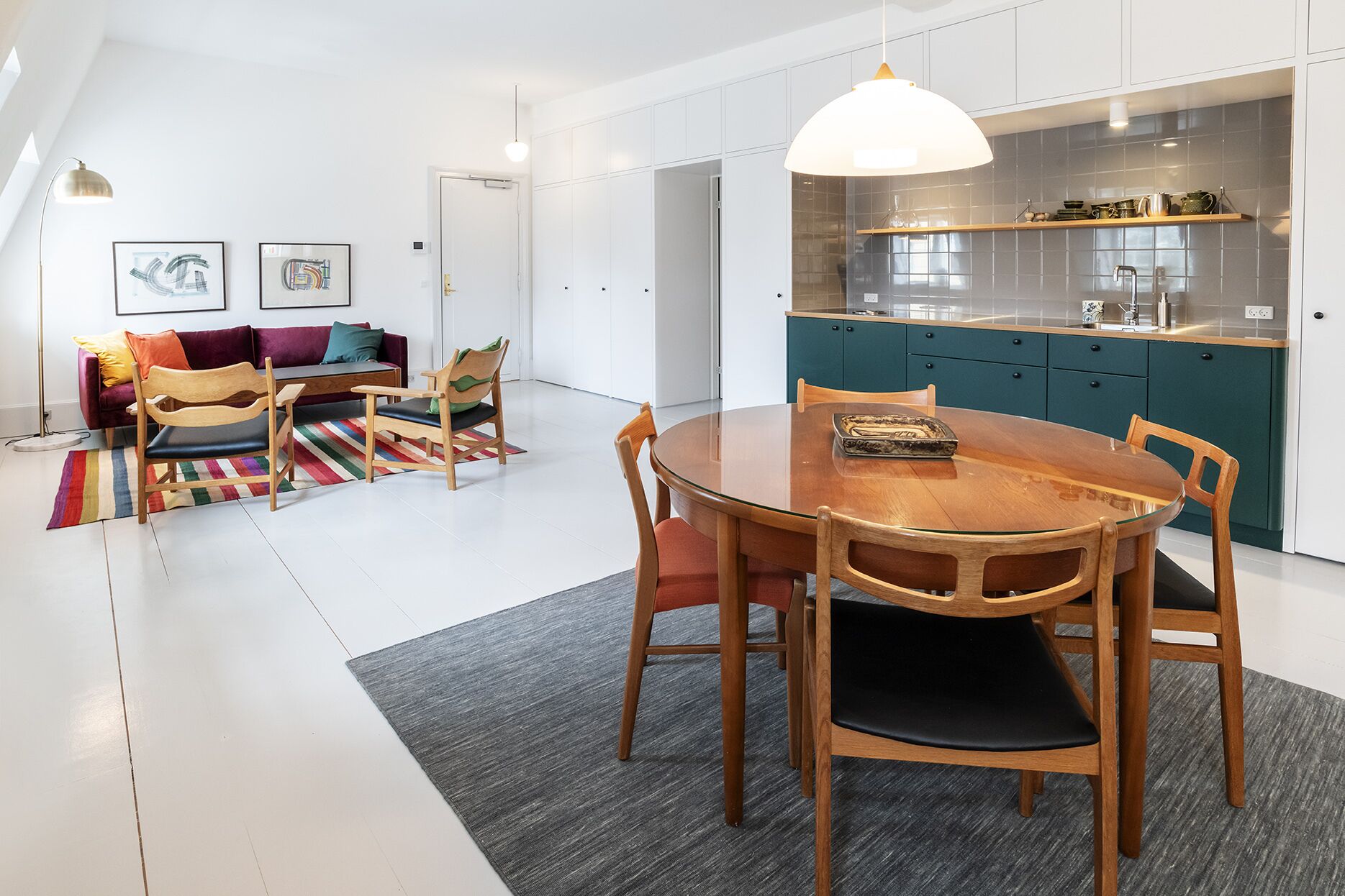 A modern kitchen with teal cabinets, a wooden dining table, and a colorful rug.