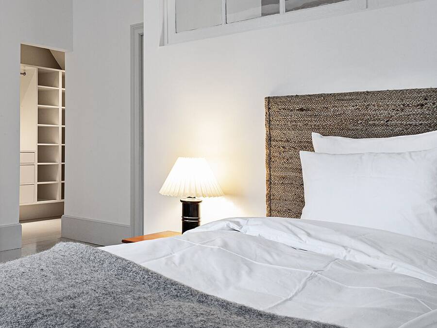 Un moderno cuarto de hotel con una cama grande, una mesita de noche con lámpara, repisas incorporadas y vista al cielo a través de una ventana.