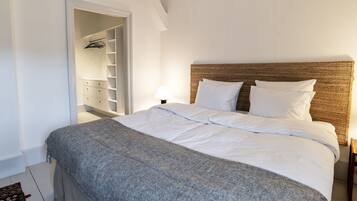 Un dormitorio con cama, mesita de noche, lámpara, armario y puerta que da a un vestidor.