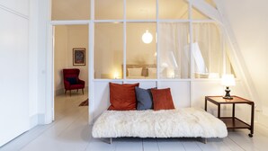 A bedroom with a large window, a bed with white and red pillows, a small side table, and a red chair. - Kanalhuset (Copenhagen)
