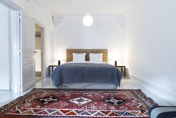 A bedroom with a bed, a nightstand, a lamp, a patterned rug, and a white door. - Kanalhuset (Copenhagen)