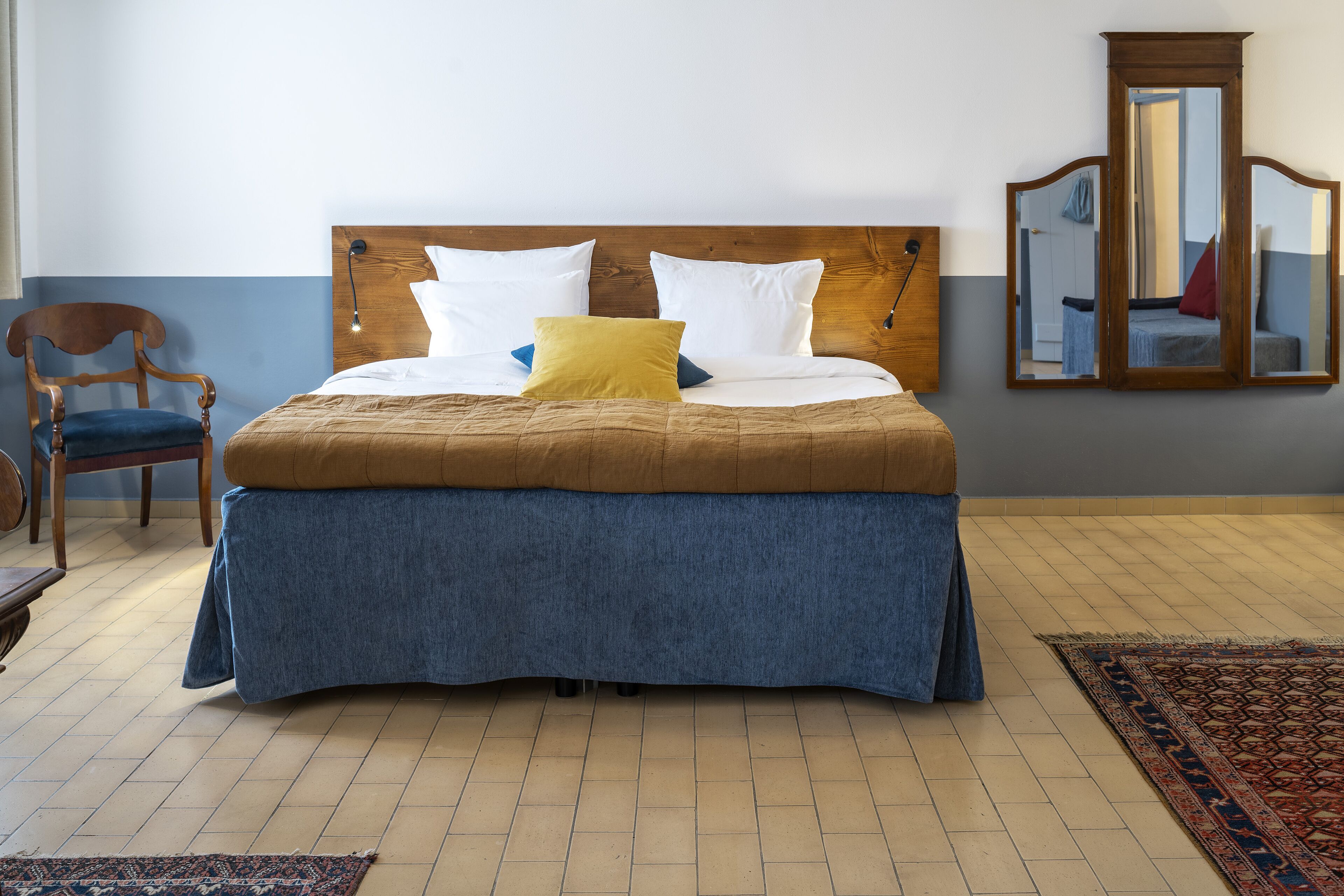 Een netjes opgemaakt bed met een houten hoofdbord, een blauw laken en meerdere kussens.