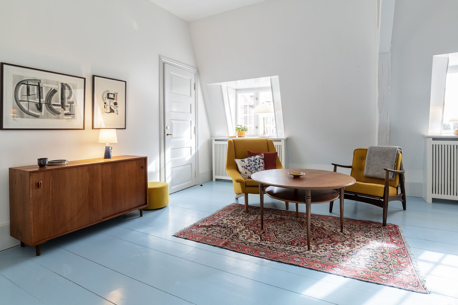 A modern living room with a wooden cabinet, a yellow armchair, a round wooden table, and a patterned rug.