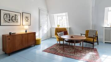 A modern living room with a wooden cabinet, a yellow armchair, a round wooden table, and a patterned rug.