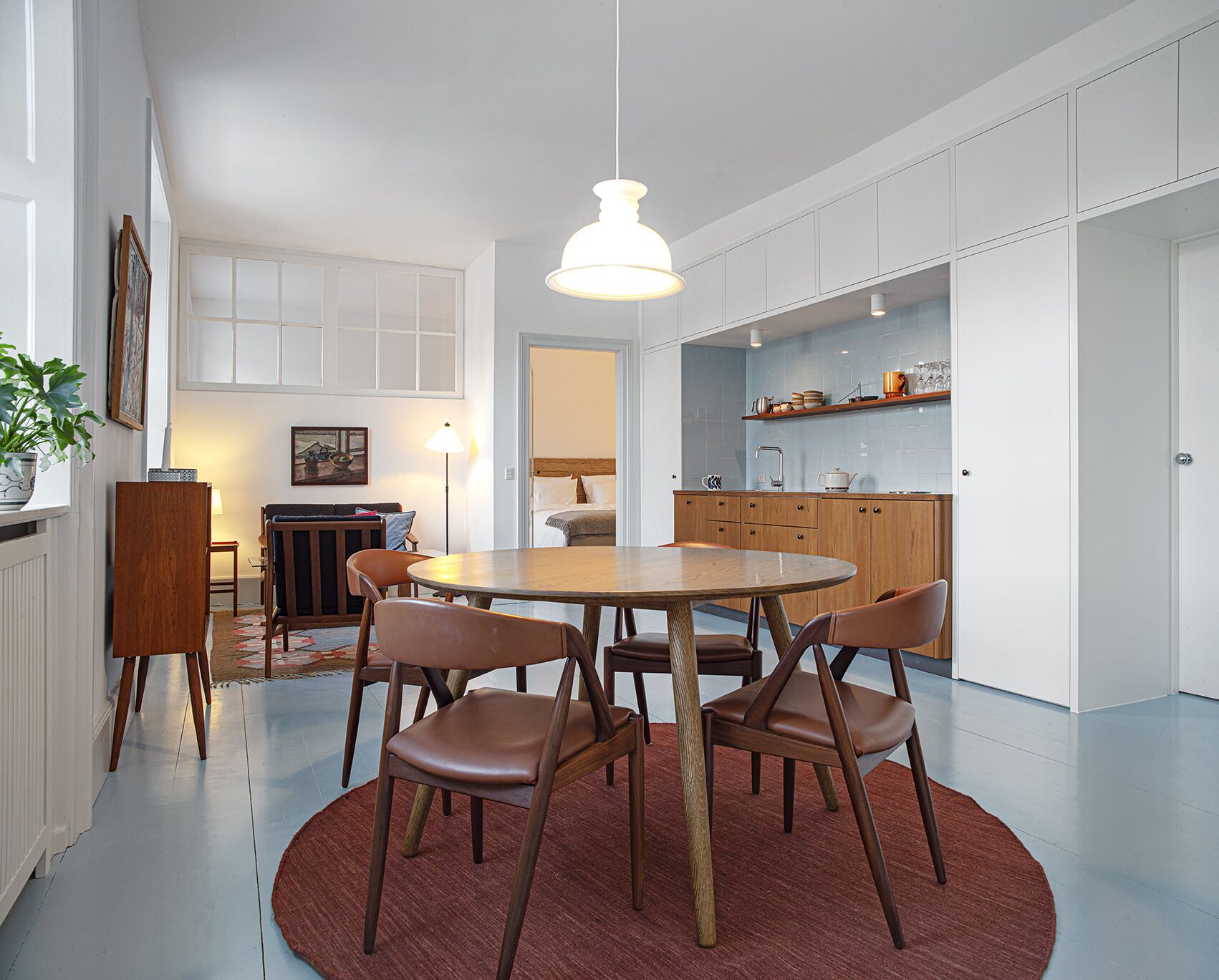 Een moderne keuken met witte kasten, een houten eettafel met vier stoelen, en een hangende hanglamp.