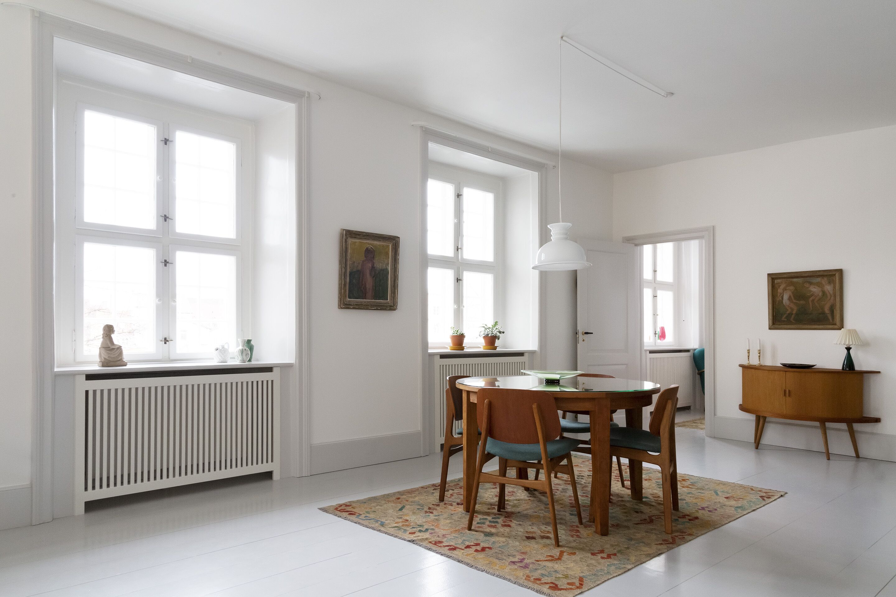 A dining area with a table and chairs, large windows, a radiator, and a cabinet.