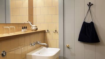 A bathroom with a white sink, beige tiles, a mirror, and a dark blue bag hanging on the wall.