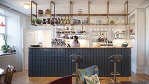 A bar area with a blue tiled counter, wooden chairs, and a person behind the bar. - Kanalhuset (Copenhagen)