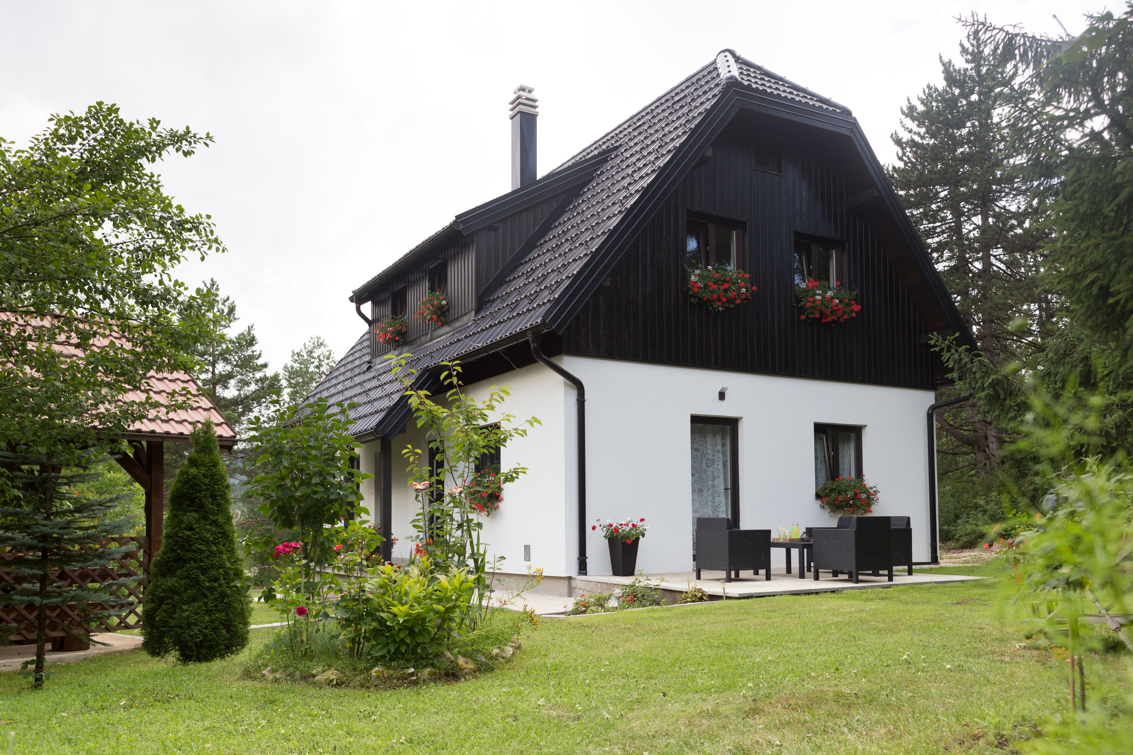 A modern two-story house with a sloped roof, a chimney, and a small porch with outdoor furniture.