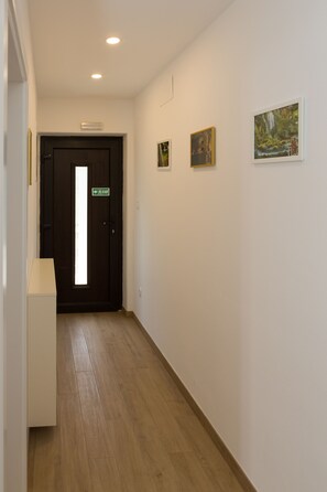 A hallway with a wooden floor, a dark door with an exit sign, and three framed pictures on the wall.