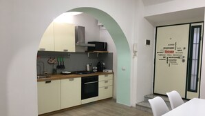 A modern kitchen with a wooden countertop, white cabinets, and a built-in oven. There is a dining area with a white table and chairs. - Casa Doria - Vatican Museums (Roma)