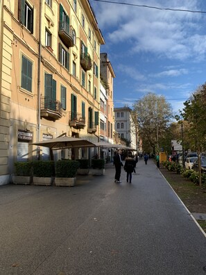 Eine Straße mit Gebäuden, Außenbestuhlung und blauem Himmel.