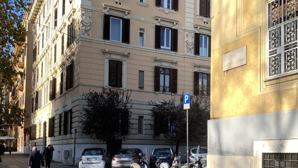 A multi-story building with classical architecture, a visible street sign, parked vehicles, and a pedestrian crossing. - Casa Doria - Vatican Museums (Roma)