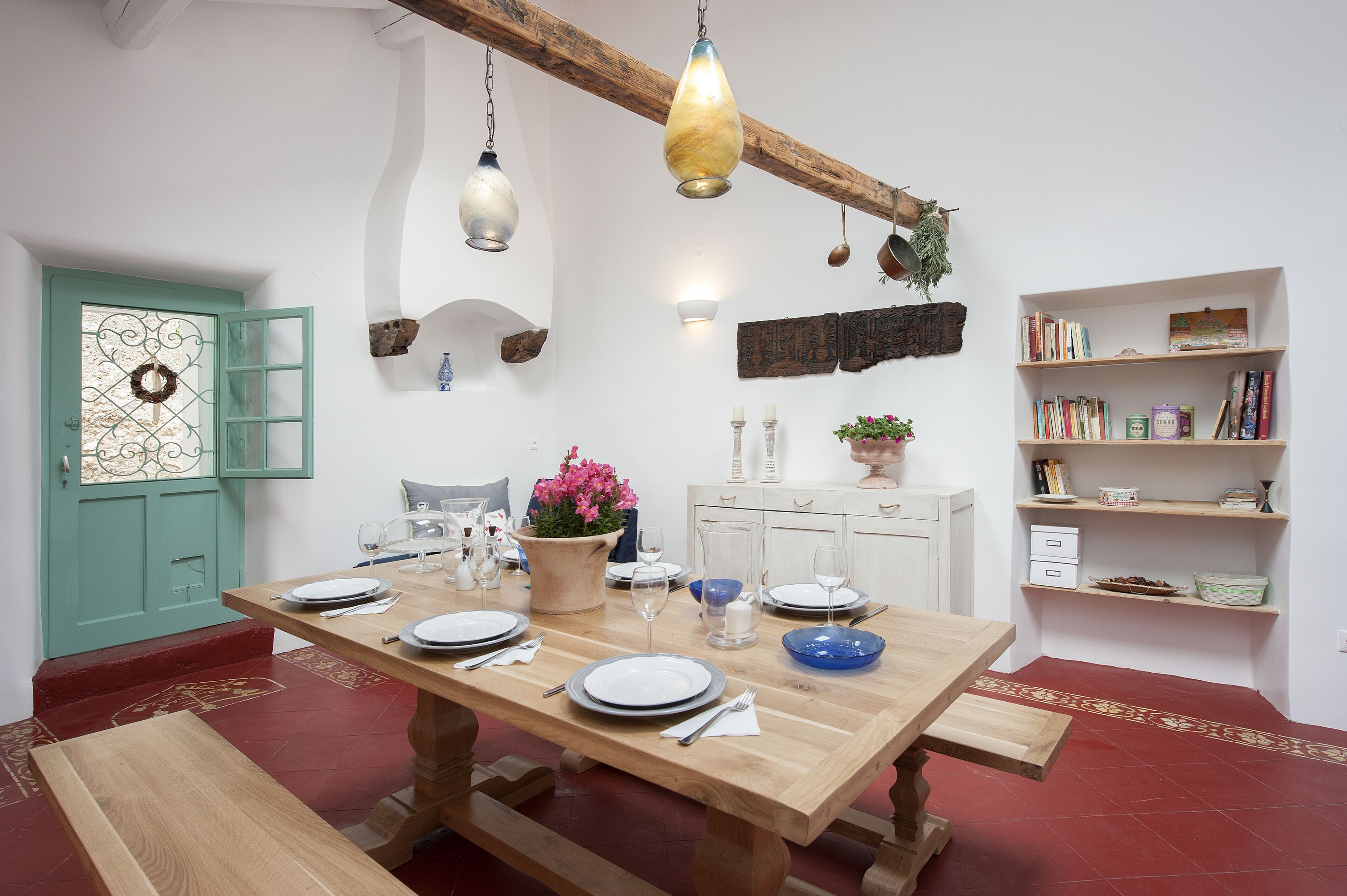 Un comedor con una mesa de madera dispuesta para cuatro, un armario blanco y una estantería con libros y objetos decorativos.