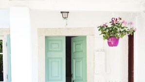 A white building with a teal door, steps leading to the entrance, and various potted plants. - White Jasmine Cottage (Corfu)