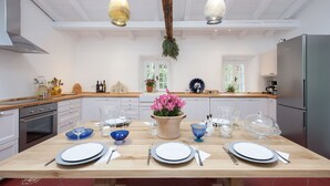 A modern kitchen with white cabinets, a wooden countertop, and a dining table set for six. - White Jasmine Cottage (Corfu)