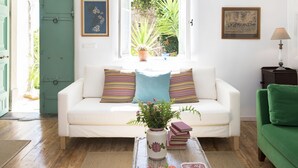 A white sofa with striped pillows, a vase with flowers, and a window with a view of greenery. - White Jasmine Cottage (Corfu)