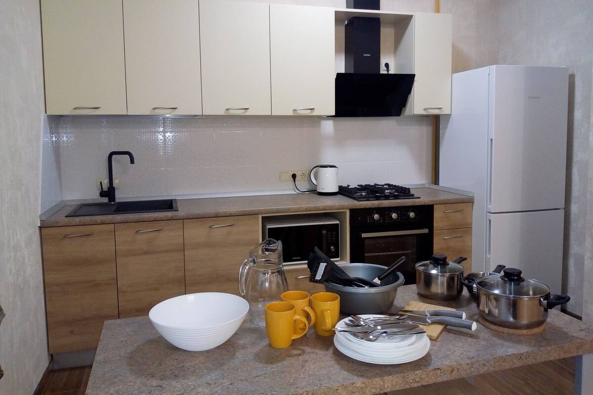 Eine Küche mit Spüle, Herd, Backofen und Kühlschrank. Im Schrank befinden sich Küchenutensilien und Geschirr, außerdem ein Kaffeeautomaten.