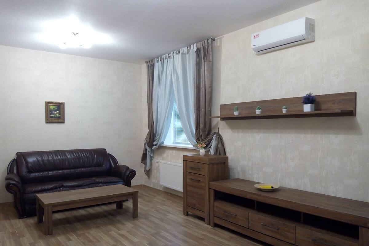 Ein Wohnzimmer mit einem Ledersofa, einem Holztisch und einer Holz-TV-Konsole mit Flachbildfernseher.