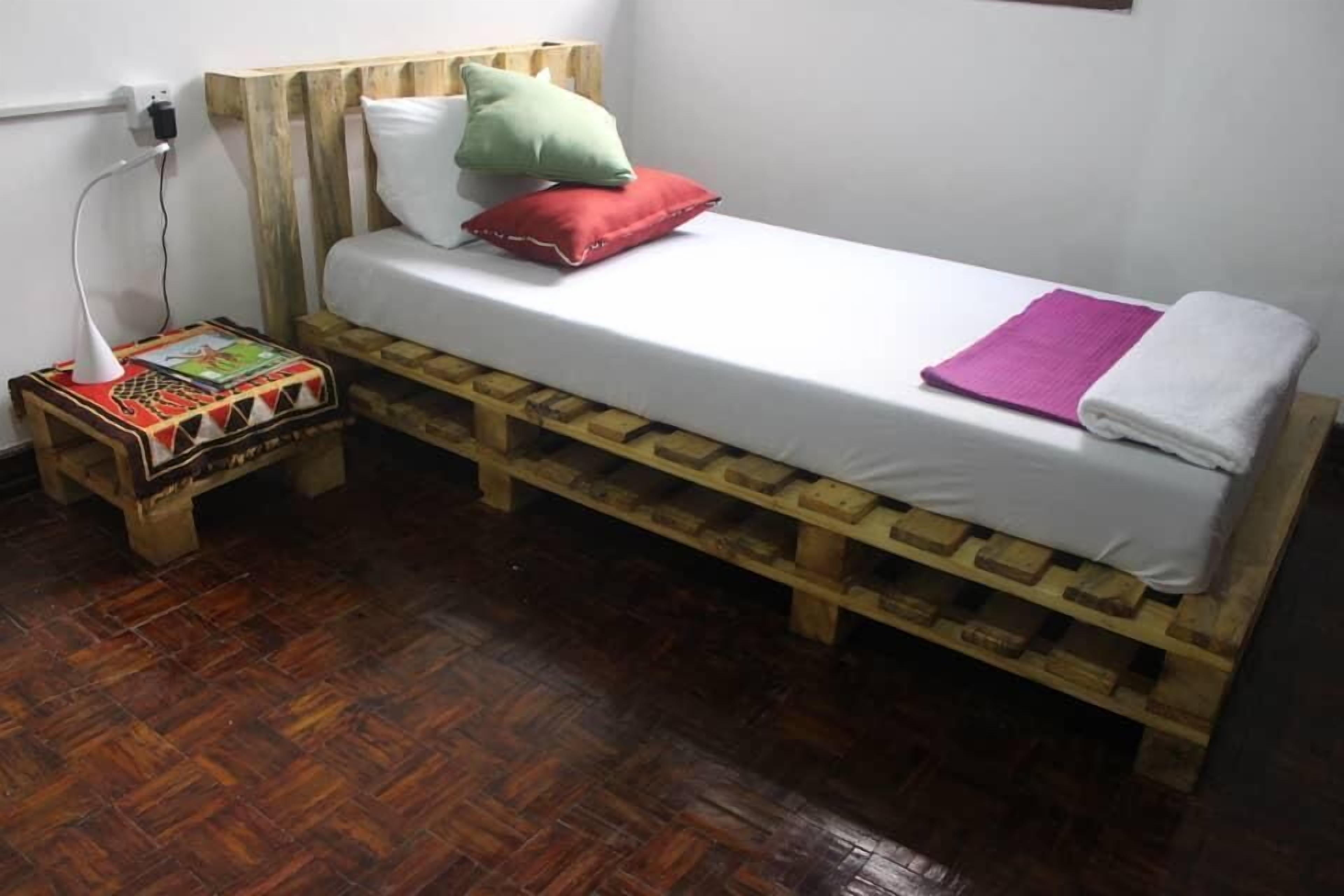 Une petite pièce rustique avec un lit en bois, une table de chevet avec une lampe et un tapis à motifs.