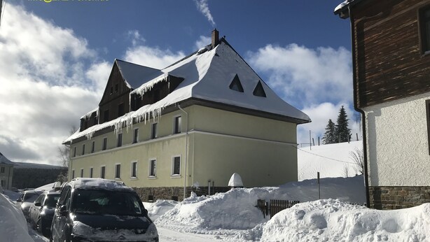 Un bâtiment enneigé, doté d’un toit en pente, avec des voitures garées et un ciel dégagé.