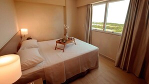 A hotel room with a bed, a bedside table with a lamp, a tray with a vase of flowers, and a window with curtains. - Condomínio Salinas Park Resort (Salinópolis)