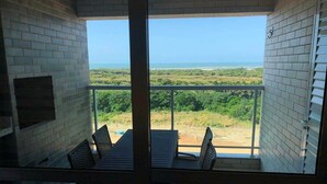 A balcony with a table and chairs, a brick wall, and a view of the ocean. - Condomínio Salinas Park Resort (Salinópolis)