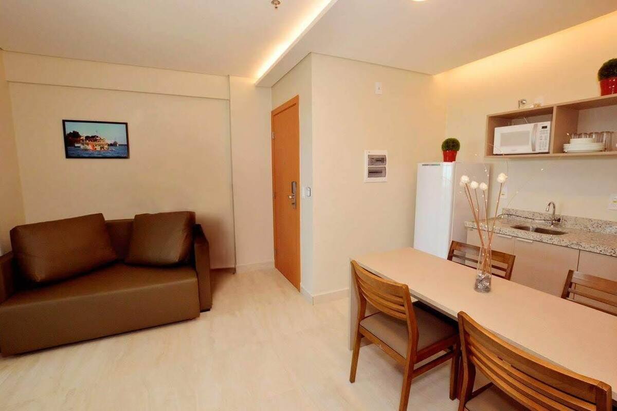 Um espaço de estar compacto com sofá, mesa de jantar, cadeiras, micro-ondas e uma pequena cozinha.