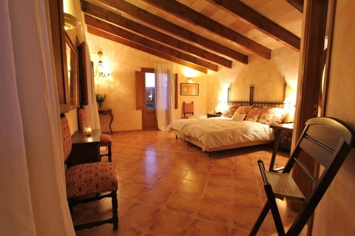 A bedroom with a large bed, a chair, a nightstand, and a window with curtains.