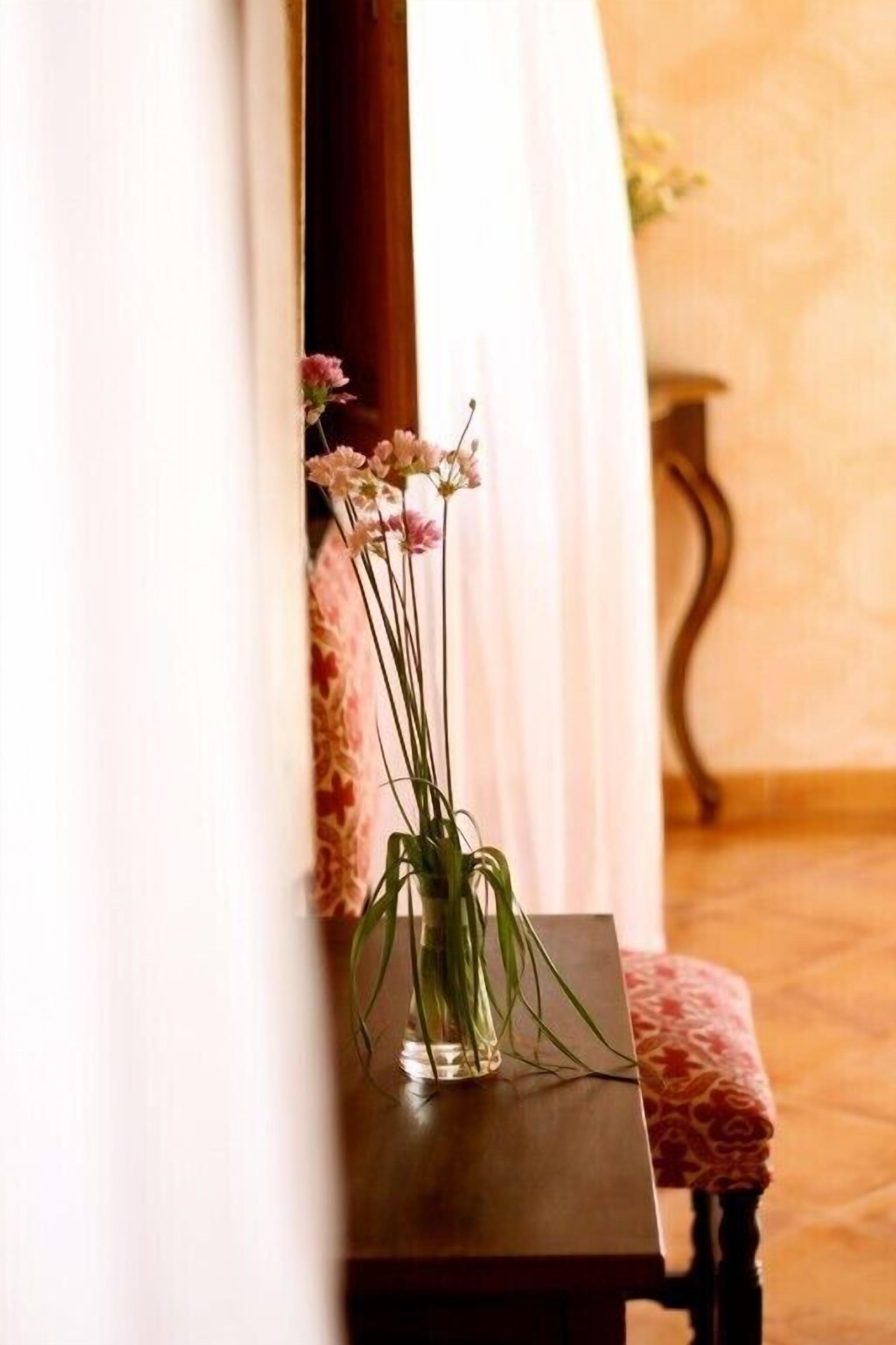 A small table with a vase of flowers in a room with a wooden floor and a patterned wall.