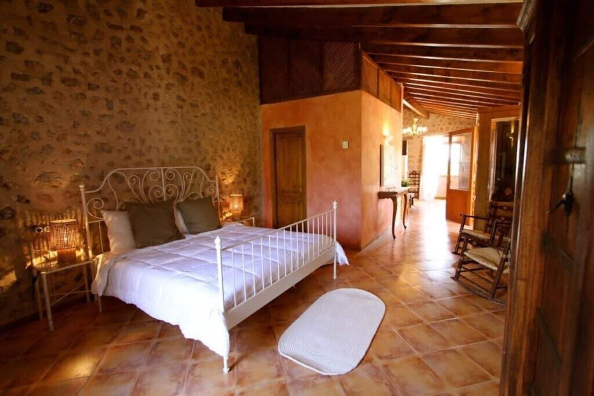 A bedroom with a stone wall, a bed with a white metal frame, a wooden floor, and a wooden ceiling.