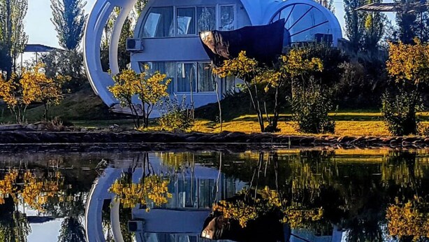 A modern building with a circular design, surrounded by trees and a body of water reflecting its structure. - La Escondida San Rafael - Cabañas (San Rafael)
