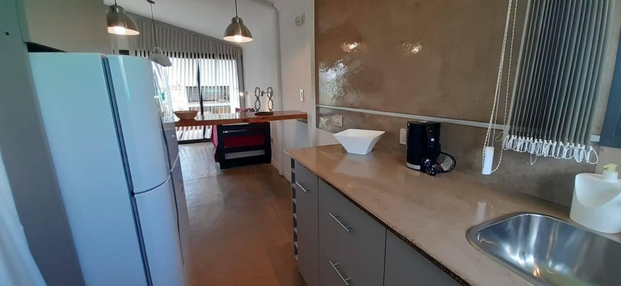 Cozinha moderna com pia de aço inoxidável, geladeira e bancada com cafeteira.