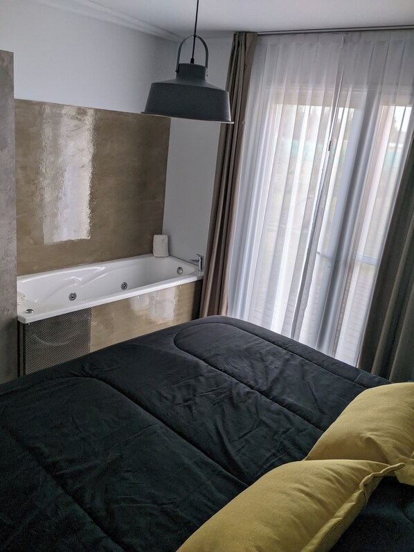 A bedroom with a bed, a hanging light fixture, a built-in shelf with a towel, and a window with curtains.
