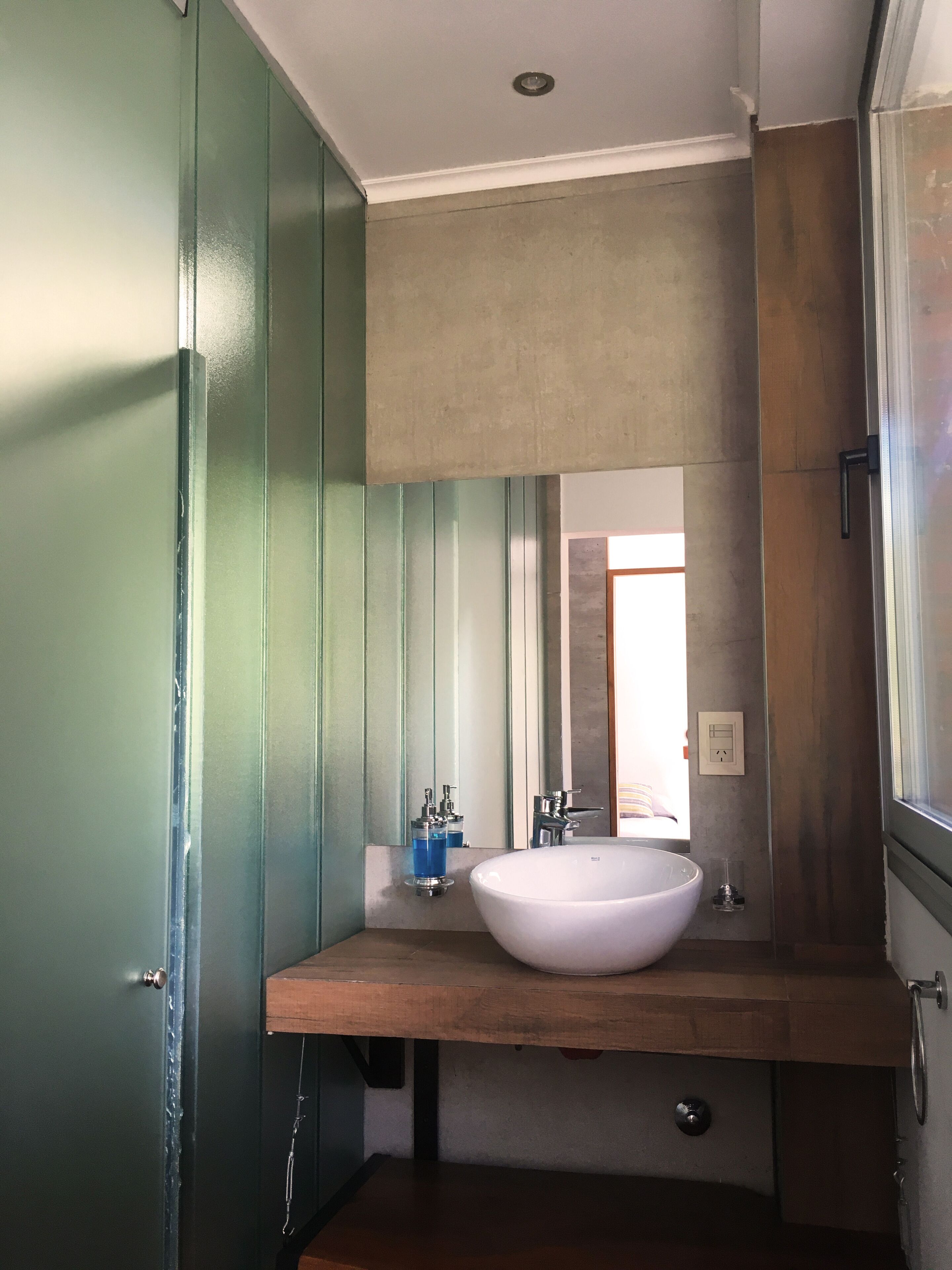 Un baño con un lavamanos grande y blanco, un espejo encima y una puerta verde.