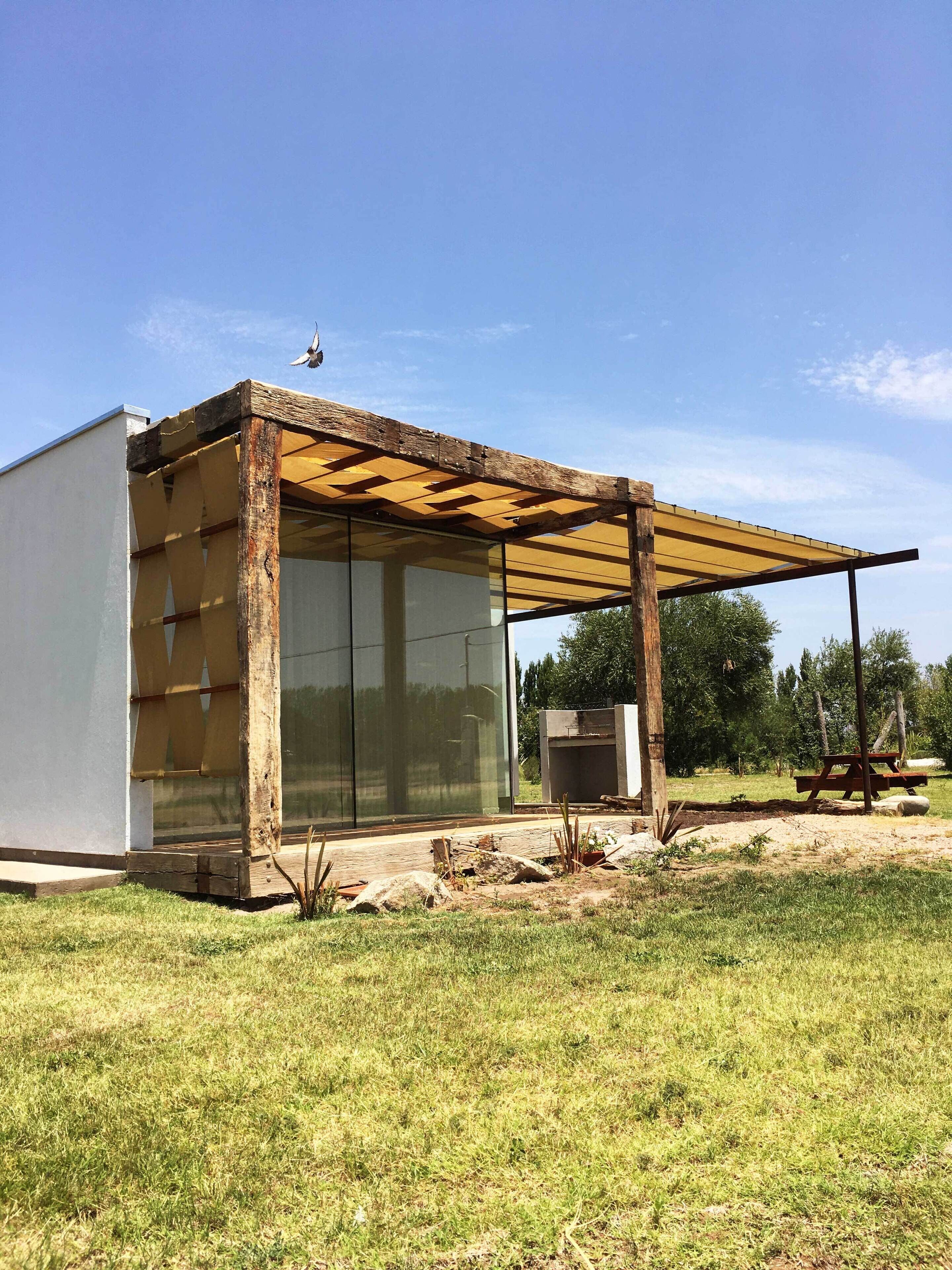 Una estructura moderna al aire libre con cerramiento de vidrio, vigas de madera y base de hormigón.