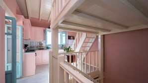 A kitchen with pink cabinets, a white staircase, and a view into the dining area. - Harmony House (Corfu)