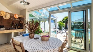 A sunlit patio with a round table, chairs, a wicker basket, and a potted plant.
