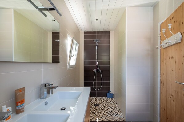 A modern bathroom with a large white bathtub, a shower with a wall-mounted faucet, and a wooden door.