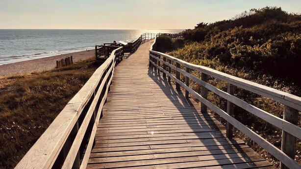 A wooden boardwalk leading to a beach with a railing on one side.